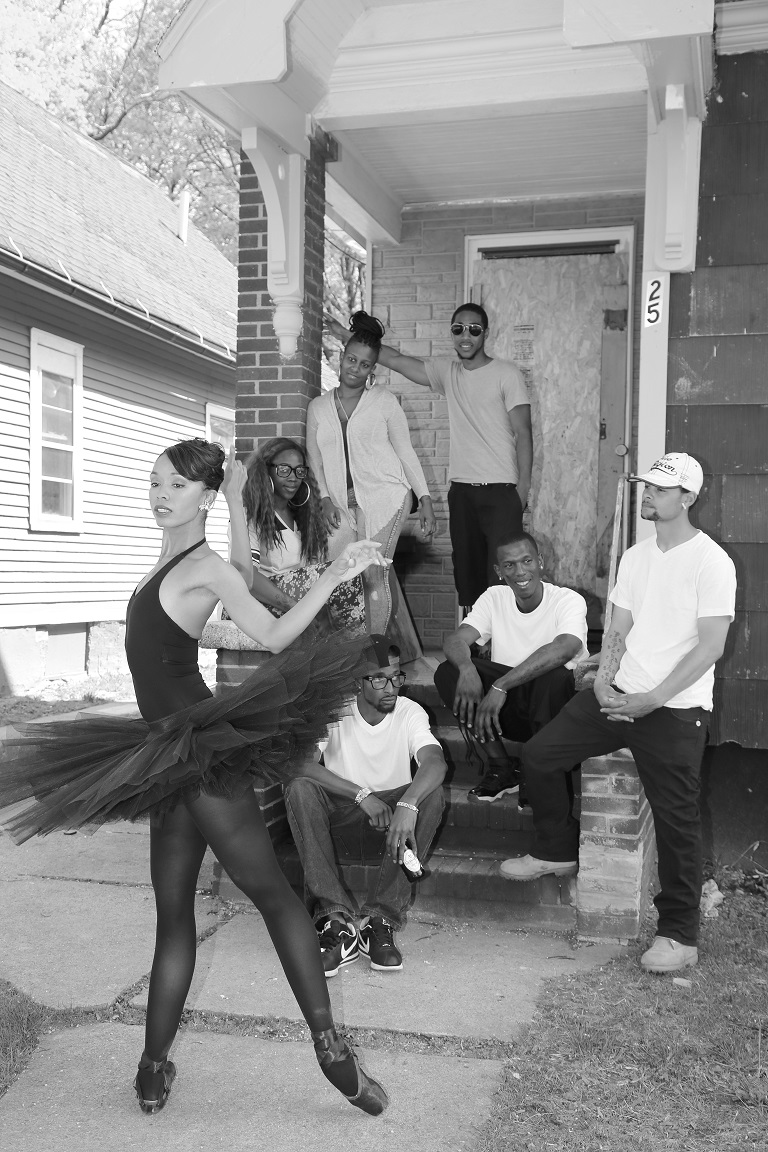 Ash in a black tutu, tights and point shoes. A group of community members of different ages observe her on a porch.